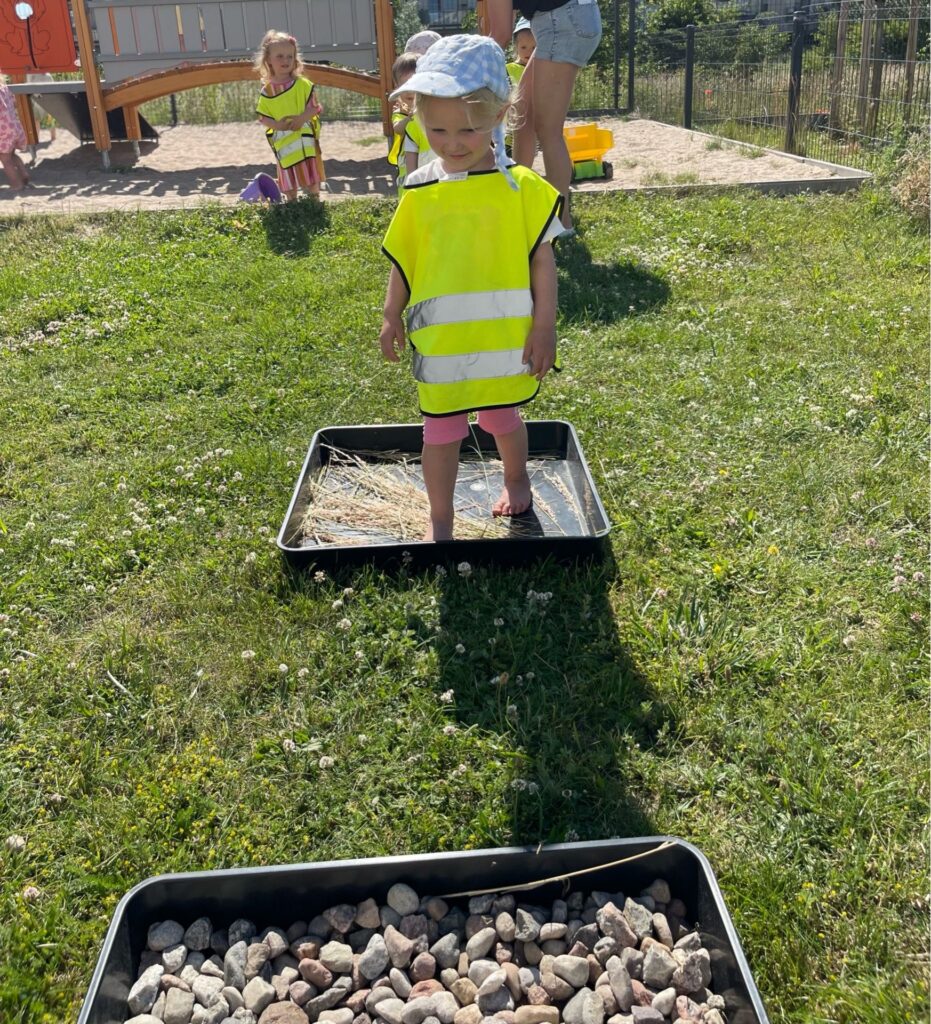 Dziecko stoi na podkładce, na której leży kępka trawy.