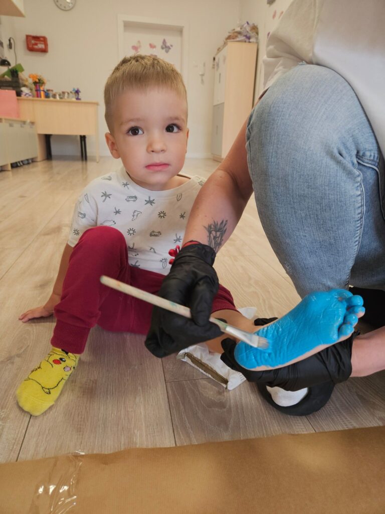 Pani maluje stopę dziecka niebieską farbą.